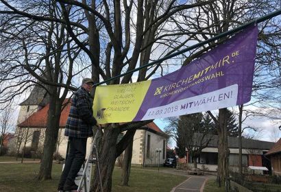 Horst Sauk wirbt für die Kirchenvorstandswahl und hängt ein Transparent vor der Martinskirche auf.