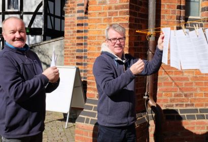Pastor Thorsten Kröncke (rechts) hängt gemeinsam mit Küster Alexander Eifold die Andachtsblätter auf die Wäscheleine vor der Elisabeth-Kirche