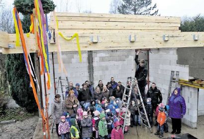 Noch regnet es hinein in den künftigen Bewegungsraum des St.-Petri- Kindergartens, den am Montag die bunten Bänder des Richtkranzes schmücken. Zimmermann Ulf Losse (auf der Leiter) schlägt mit dem Hammer auf Holz. Bild: Lauber