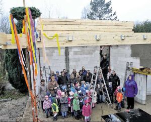 Noch regnet es hinein in den künftigen Bewegungsraum des St.-Petri- Kindergartens, den am Montag die bunten Bänder des Richtkranzes schmücken. Zimmermann Ulf Losse (auf der Leiter) schlägt mit dem Hammer auf Holz. Bild: Lauber
