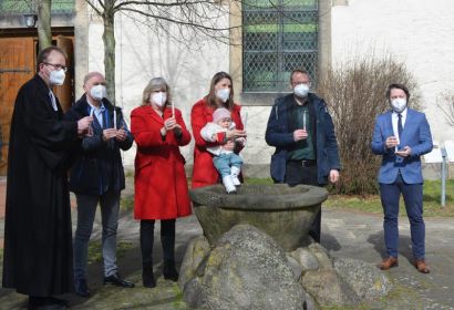 Pastor Rainer Müller-Jödicke (von links), Wolfgang und Gabriela Kasten, Jana, Mila Marie und Benjamin Buske und Diakon Merlin Langrehr geben das Osterlicht am Taufstein vor der Engelbosteler Martinskirche weiter . Foto: Andrea Hesse