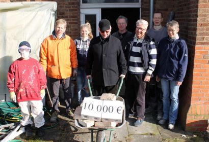 Kurt Hoffmann (mit Schubkarre) und der Vereinsvorsitzende Jörg Klabunde (rechts daneben) überreichen die Spende in Höhe von 10.000 Euro für den Ausbau des Jugendraumes symbolisch an Lisa Sacht (rechts). Foto: Friedrich Bernstorf