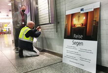 Flughafenpastor Karl-Martin Harms schaut zu, während Thomas Wesner den Reisesegen montiert. Foto: Andrea Hesse
