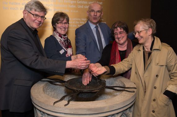Superintendent Holger Grünjes (Mitte) mit Landessuperintendentin Petra Bahr (rechts) und weiteren Teilnehmenden des Ephoren-Konvents an dem alten Taufstein. Foto: Johannes Neukirch