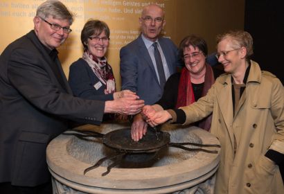 Superintendent Holger Grünjes (Mitte) mit Landessuperintendentin Petra Bahr (rechts) und weiteren Teilnehmenden des Ephoren-Konvents an dem alten Taufstein. Foto: Johannes Neukirch