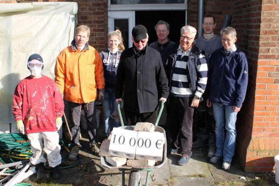 Kurt Hoffmann (mit Schubkarre) und der Vereinsvorsitzende Jörg Klabunde (rechts daneben) überreichen die Spende in Höhe von 10.000 Euro für den Ausbau des Jugendraumes symbolisch an Lisa Sacht (rechts). Foto: Friedrich Bernstorf